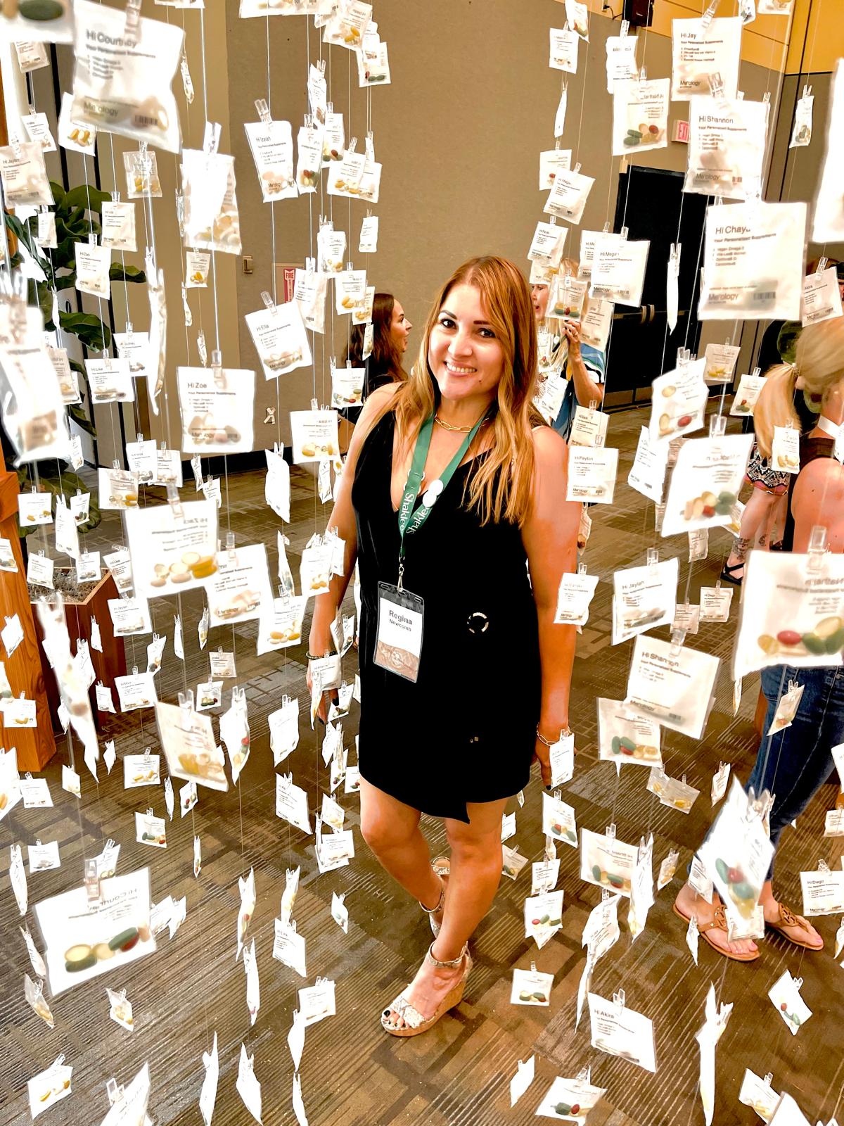 Regina posing in the middle of many hanging vitamin packs